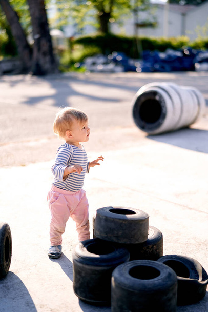 駐車場の積み重ねられた車のタイヤの横に子供が立っている - 写真・画像