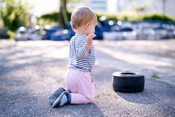 Niño se arrodilla cerca de un borde de coche en un estacionamiento - Foto, Imagen