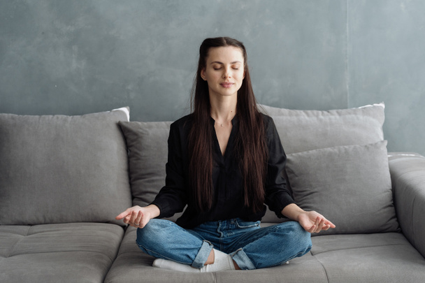Розслаблена спокійна молода жінка медитує, сидить на дивані комфорту у вітальні, відчуває втому після роботи, відпочиває в затишному будинку у вихідні, насолоджується благополуччям дихальних вправ
 - Фото, зображення