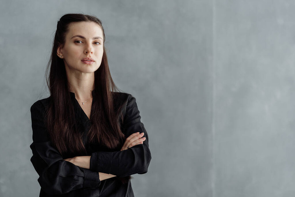Business portrait of young confident woman looking at camera, crossed hand on chest, standing against copy space wall. Successful businesswoman in formal wear on grey background - Фото, зображення