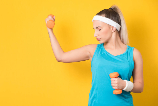 Sporty girl training gym with dumbbell, isolated on yellow background. Half length of fit sportswoman lifting weights. Fitness motivation. 80s styling. Studio shot - Φωτογραφία, εικόνα
