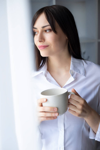 beautiful woman holding cup and looking at window - Photo, Image