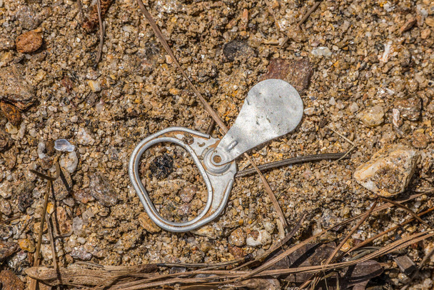 Old style pull tab from a soda or beer can laying upside down on the beach at the lake polluting the environment on a bright sunny day in springtime closeup view - Photo, Image