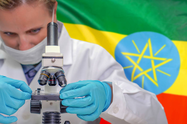 Biochimiste féminine regardant à travers un microscope sur fond de drapeau éthiopien. Technologie médicale et recherche pharmaceutique et développement de concepts scientifiques en Éthiopie - Photo, image
