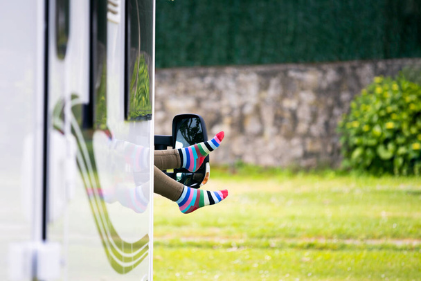 Pieds avec des chaussettes colorées amusantes qui sortent de la fenêtre d'un camping-car. Conceptuel de voyage, vacances, repos - Photo, image