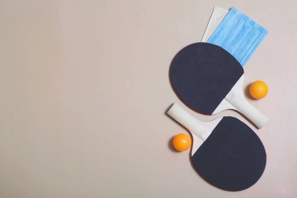 ベージュの背景にテニスラケット、ボールと医療用マスクのトップビュー。隔離中の屋外エンターテイメント、パンデミック. - 写真・画像