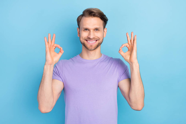Photo portrait of man showing okay gesture with both hands smiling in purple clothes isolated on pastel blue color background - Zdjęcie, obraz
