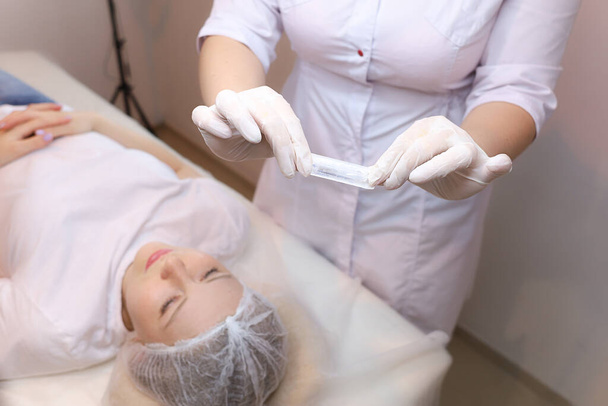 The cosmetologist holds a sterile bag with a needle in front of the client thus showing him the process of removing it from the bag - Photo, Image