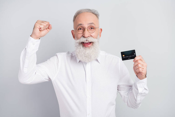 Photo of aged man happy positive smile hold credit card rejoice victory success fists hands isolated over grey color background - Foto, afbeelding