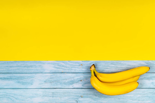 Yellow bananas lie on a blue wooden background and a yellow background. - Fotoğraf, Görsel