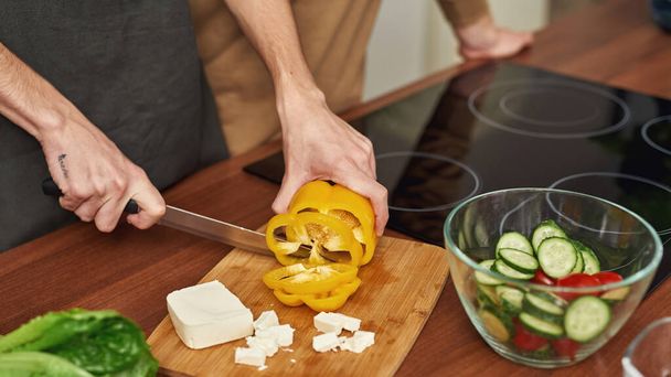 Man cutting yellow pepper for salad in modern kitchen, - 写真・画像