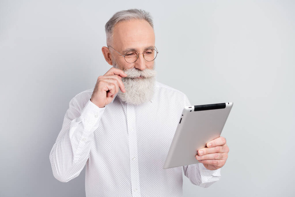 Photo of attractive focused happy old man look hold tablet touch mustache isolated on grey color background - Фото, изображение