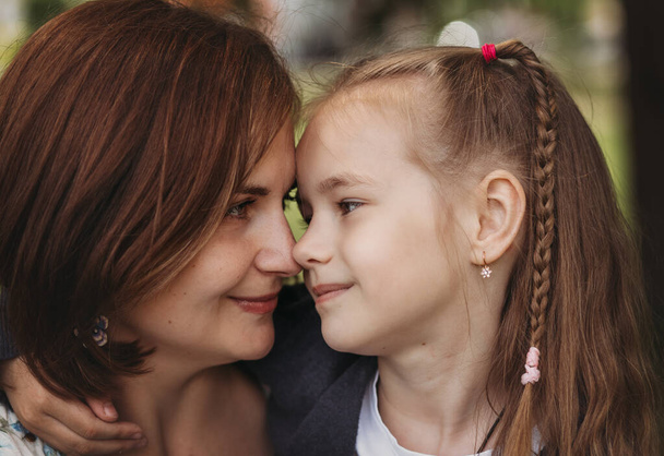 Mom and daughter look at each other. A close-up portrait of a woman and a child - Фото, изображение