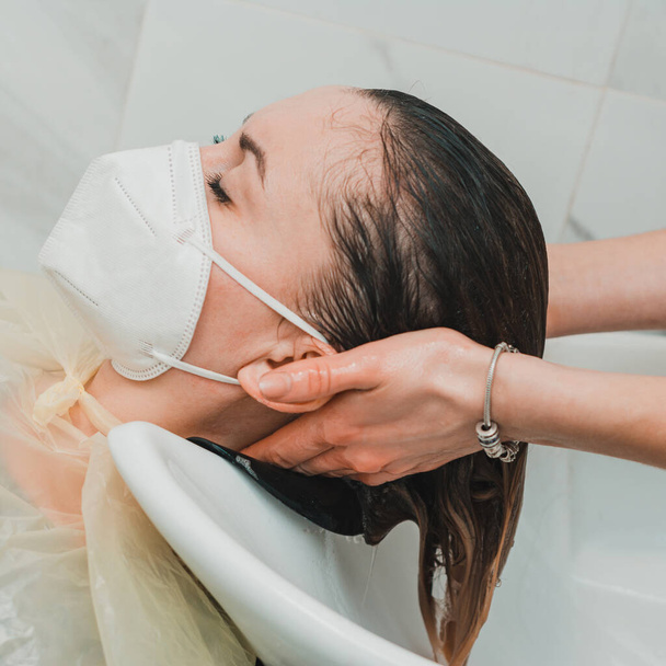 Parrucchiere durante la quarantena mondiale, lavando la testa in un salone di bellezza, un cliente in maschera. nuovo - Foto, immagini