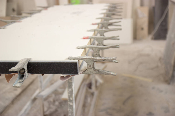 Bevestiging van twee oppervlakken aan de tafel van een timmerman met een klem voor het betrouwbaar verlijmen van twee ongelijke oppervlakken tijdens de individuele meubelproductie - Foto, afbeelding