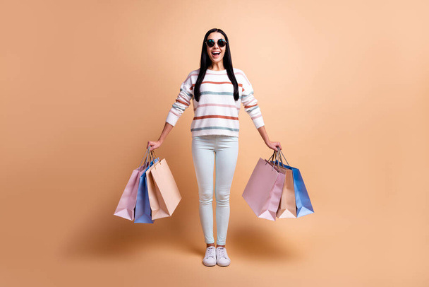 Full body photo of young excited girl happy positive smile shop black friday bags isolated over beige color background - 写真・画像