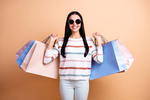 Photo of young beautiful cheerful smiling positive girl in sunglasses hold shopping bags isolated on beige color background - Fotó, kép