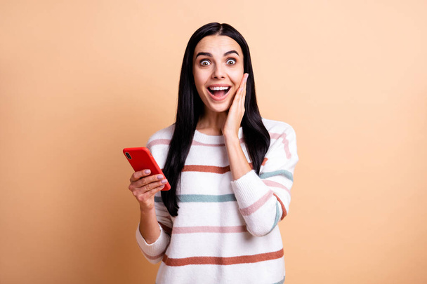 Фотографія молодої збудженої дівчини вражена шокованими здивованими продажами новин використовуйте мобільний телефон ізольований на бежевому кольоровому фоні
 - Фото, зображення