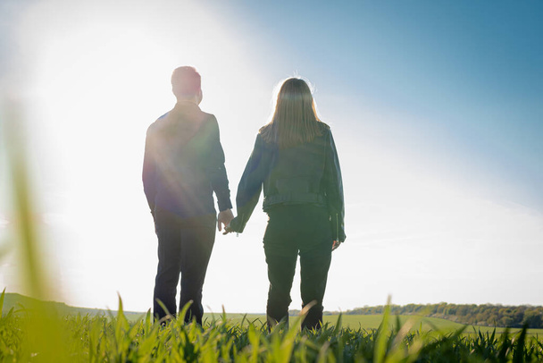 Young couple standing with their backs enjoying the sunset of a sunny field. Low key - Foto, afbeelding
