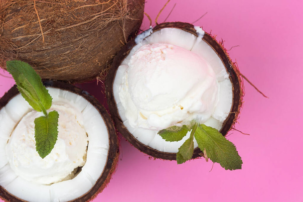 Vanilla ice cream balls in fresh coconut halves decorated with mint leaves on a pink background. - Foto, Imagem
