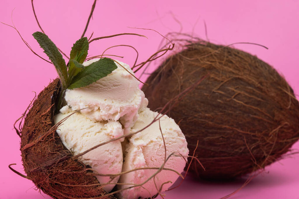 Vanilla ice cream balls in an empty coconut decorated with mint leaves on a pink background. - Foto, Imagem