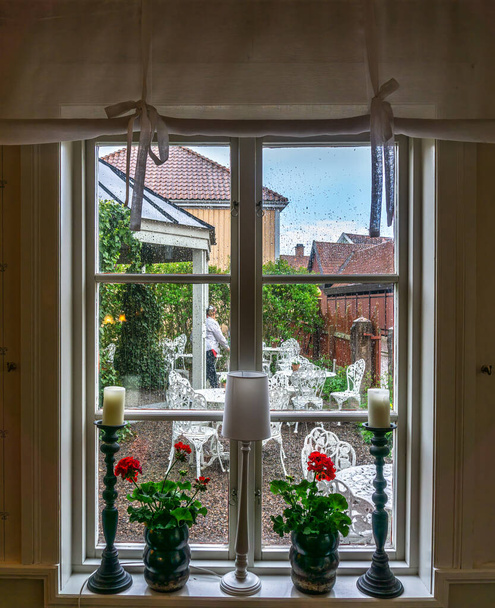 Vadstena, Szwecja - 23 maja 2021: Przytulne, urządzone okno z widokiem na podwórko podczas padającego deszczu - Zdjęcie, obraz