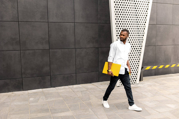 young african american man with laptop walking in the city - Foto, afbeelding