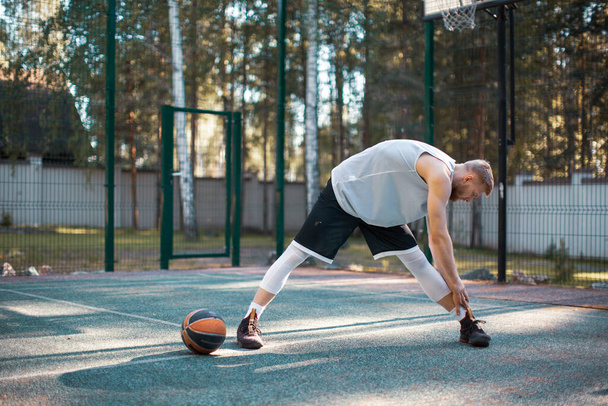 Professional male american basketball player exercising, warming up on court outdoors in summer - Foto, afbeelding