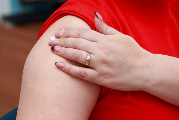 Пациент держит руку на месте инъекции во время нажатия на пластырь. Настоящая вакцинация против коронавируса ковида-19. Фон - Фото, изображение