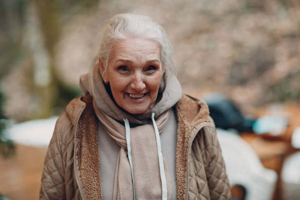 Портрет улыбающейся счастливой пожилой женщины под открытым небом и смотрящей в камеру. - Фото, изображение