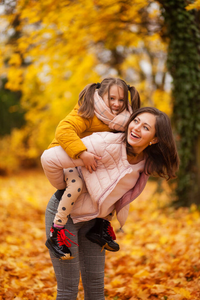mom and daughter hug and smile in the autumn park with yellow leaves, mom and daughter family relationships, walk in the park - 写真・画像