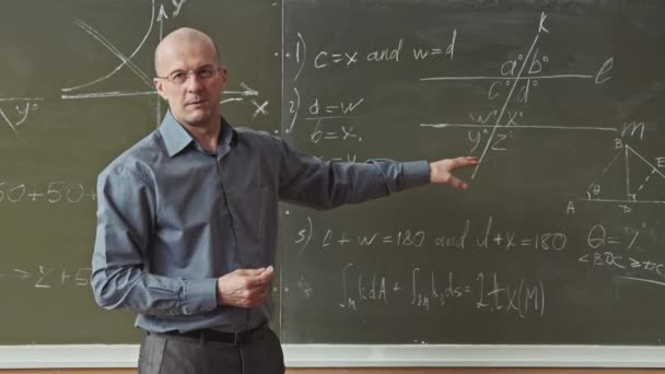 Medium slowmo van mannelijke mid-adult professor in slimme casualwear staan op blackboard kijken naar u uit te leggen hoe geometrie problemen op te lossen - Video