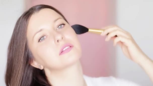 Γυναίκα με πινέλο καλλυντικών που εφαρμόζει μακιγιάζ και χαμογελαστό, προσωπογραφία ομορφιάς του καυκάσιου γυναικείου μοντέλου σε ροζ φόντο, φυσική ιδέα make-up, καλλυντικά και προϊόντα περιποίησης δέρματος εμπορική - Πλάνα, βίντεο