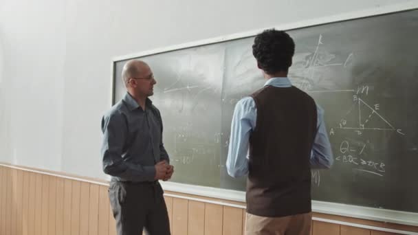 Aerial średnio powolne ujęcie samca Mieszane wyścigu student odpowiadający na tablicy próbuje rozwiązać problem twardej geometrii z pomocą profesora mid-adult - Materiał filmowy, wideo