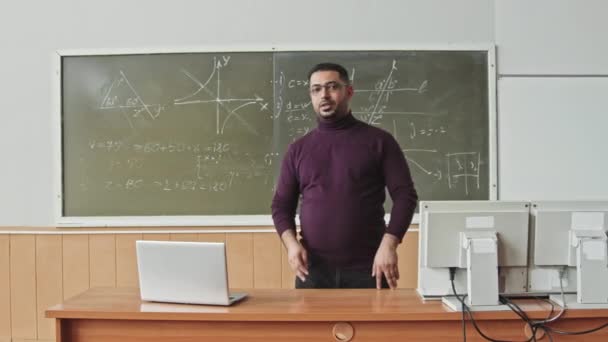 Medium slowmo of male Mixed-race mid-adult professor standing at blackboard looking at you while explaining how to solve Geometry problems - Záběry, video