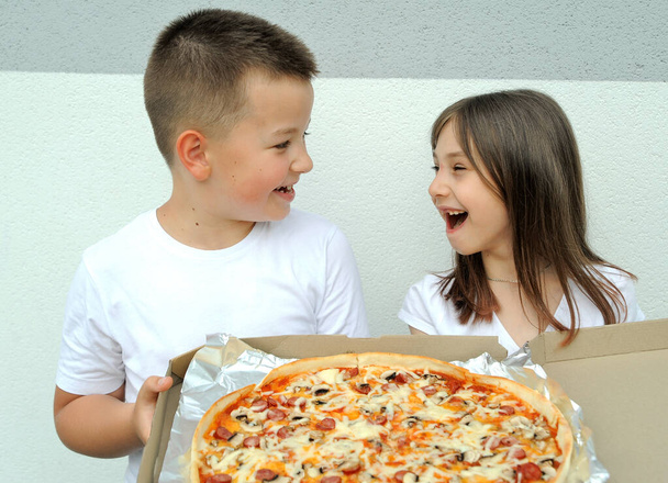 Een meisje en een jongen kijken naar grote heerlijke pizza in een doos op straat.  - Foto, afbeelding
