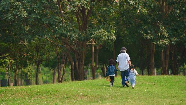 grand father holding hands of grandson and granddaughter walking together outdoors in park during summer vacation. concept of multi generation family lifestyle - Photo, image