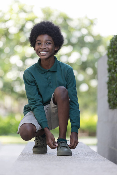 黒い巻き毛のアフリカの少年は、屋外で靴ひもで鉄の手すりに座っています. - 写真・画像