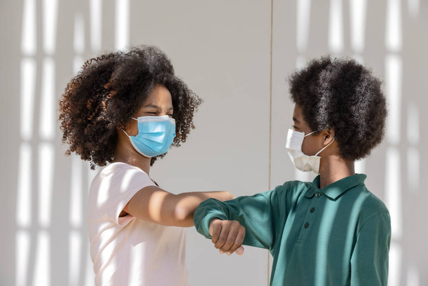 Afro gyerekek göndör haj védő maszkok együtt alatt árnyékos ereszték épület, Az emberek viselnek védő arc maszkok, hogy megakadályozzák a koronavírus terjedését. - Fotó, kép