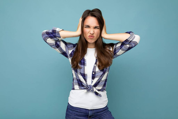 Dont want to hear it. Young emotional dissatisfied beautiful brunette woman wearing check shirt isolated on blue background with copy space and covering ears - Foto, Imagem