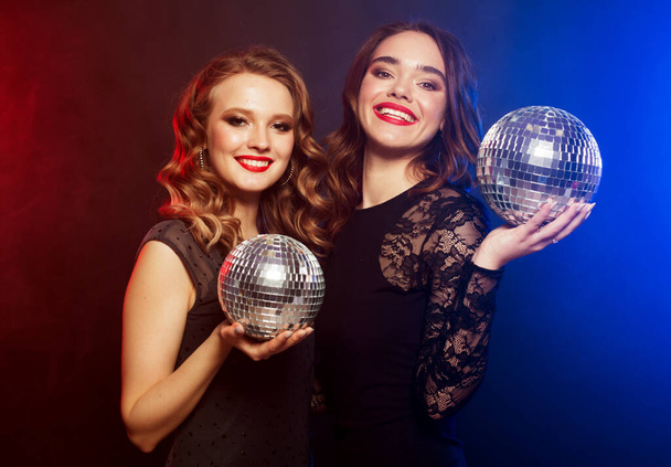 party, emotion and people concept: Two women with disco balls over blue background - Foto, afbeelding