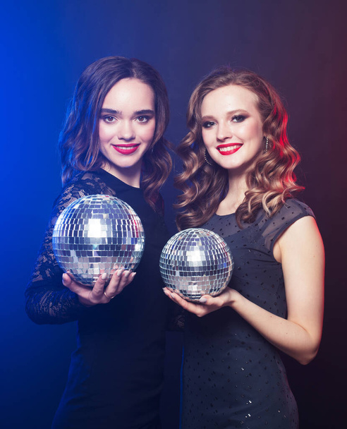 party, emotion and people concept: Two women with disco balls over blue background - Fotó, kép