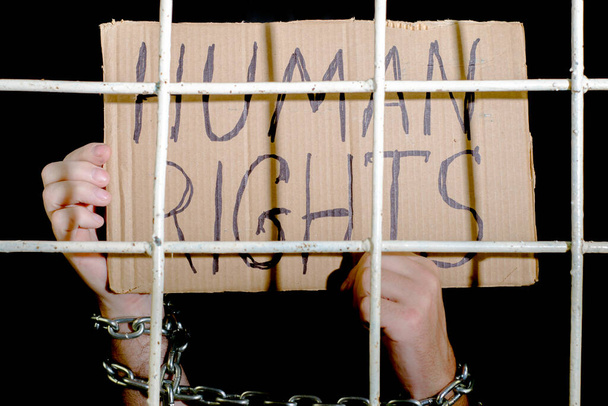 koncepcja praw człowieka wolność słowa ręce przykute żelaznym łańcuchem posiadają kartonowy znak z napisem "prawa człowieka za żelazną kratą". Wysokiej jakości zdjęcie - Zdjęcie, obraz