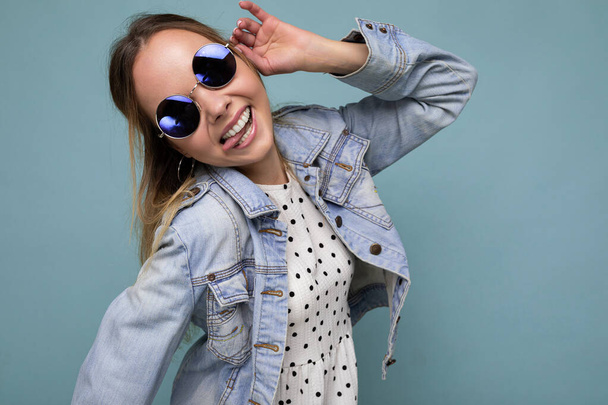 Photo shot of beautiful positive young blonde woman wearing summer casual clothes and stylish sunglasses isolated over colorful background looking at camera and having fun - Valokuva, kuva