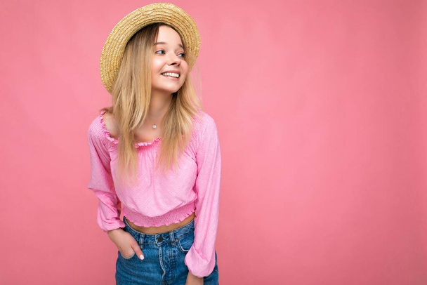 Photo of pretty young female person wearing pink blouse and beige summer hat isolated over pink background looking to the side smilimg and having fun - Photo, Image