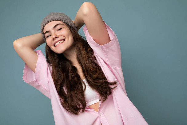 Atraktivní usmívající se šťastná mladá brunetka žena stojící izolované přes barevné pozadí zdi na sobě každodenní stylový outfit ukazující emoce obličeje při pohledu do kamery - Fotografie, Obrázek