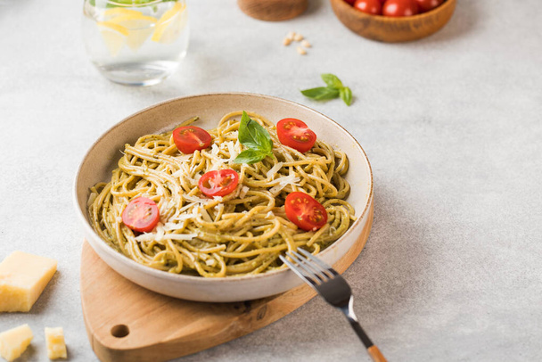 Spaghetti pasta with pesto sauce, parmesan cheese and cherry tomatoes on a plate. Menu, Italian cuisine. Copy space. - Foto, afbeelding