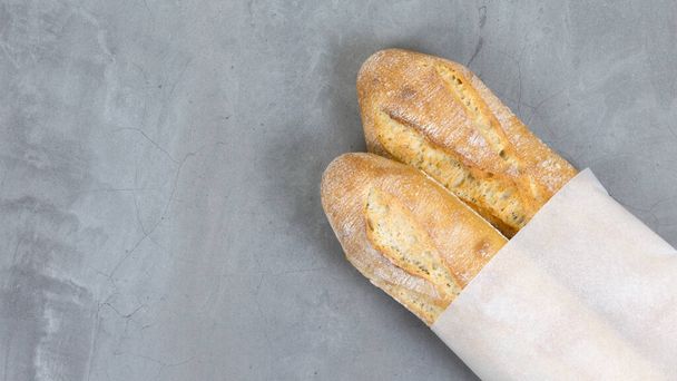 zavřít podrážděné francouzské bagety, pečený chléb na šedém kamenném stole na pozadí. ekologický papírový obal. kopírovat prostor - Fotografie, Obrázek