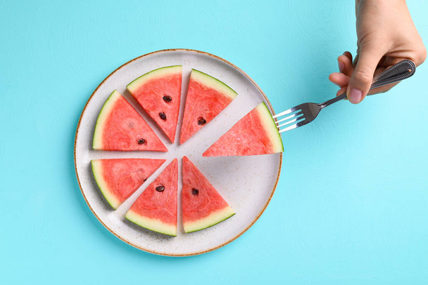 Geschnittene Wassermelonenfrüchte mit Handgabel und Essen auf Teller mit farbigem Hintergrund, Tropische Früchte, Sommersaison - Foto, Bild