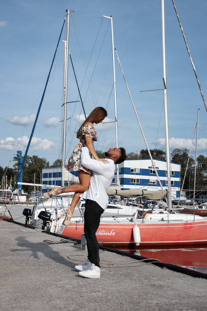 Side view of cheerful couple in love hugging in harbor with boats on sunny day in summer - Photo, Image